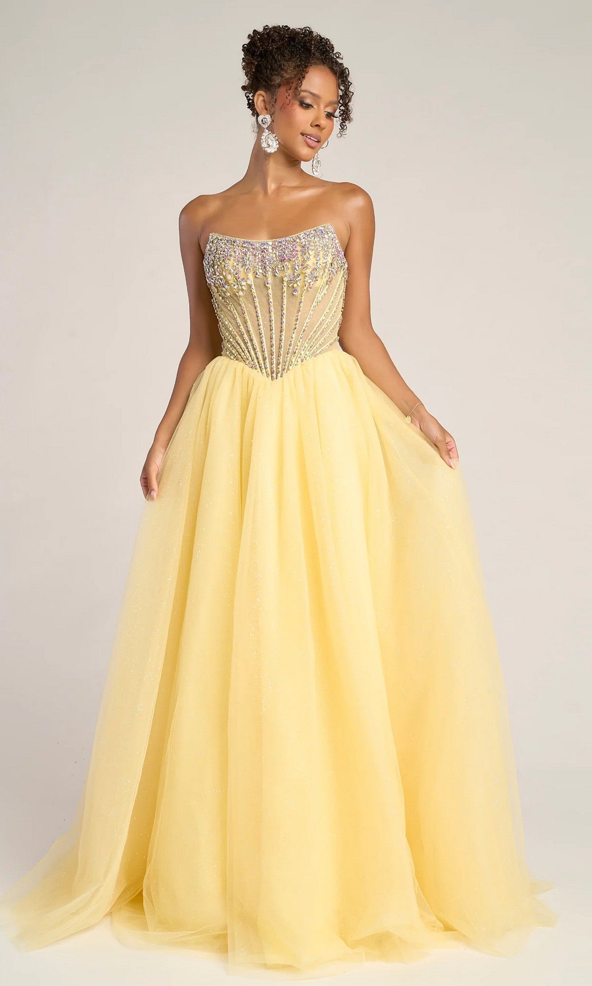 A woman models the Portia and Scarlett XO047 long formal dress, featuring a strapless yellow tulle ball gown with a beaded corset bodice and full skirt. Ideal as an elegant prom dress, shown against a plain background.
